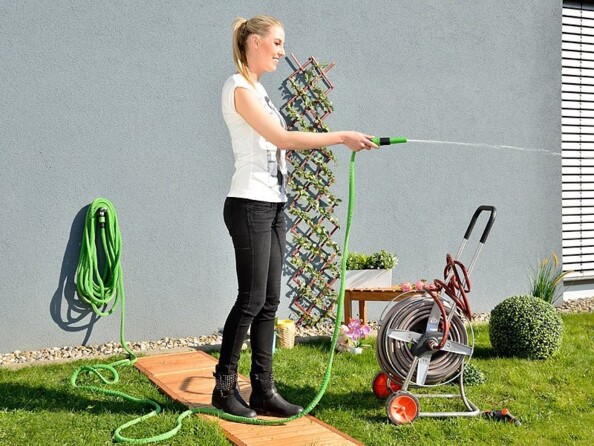 Femme arrosant son gazon à l'aide d'une lance de pulvérisation et du tuyau d'arrosage extensible