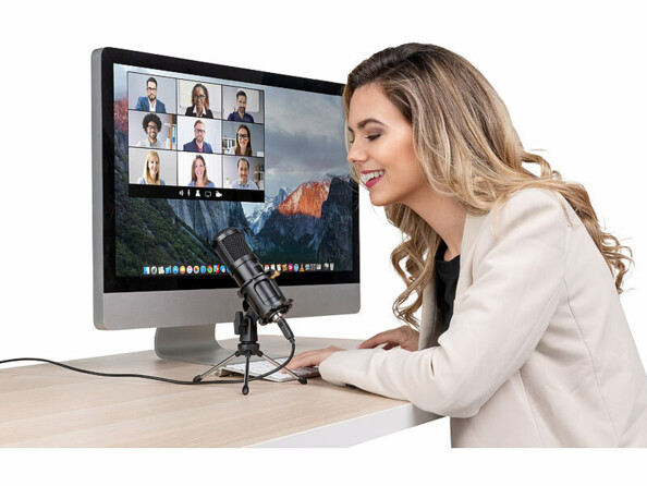 Femme assise à un bureau et parlant devant le micro filaire sur trépied devant un écran d'ordinateur type MacBook allumé sur une plateforme de réunion professionnelle