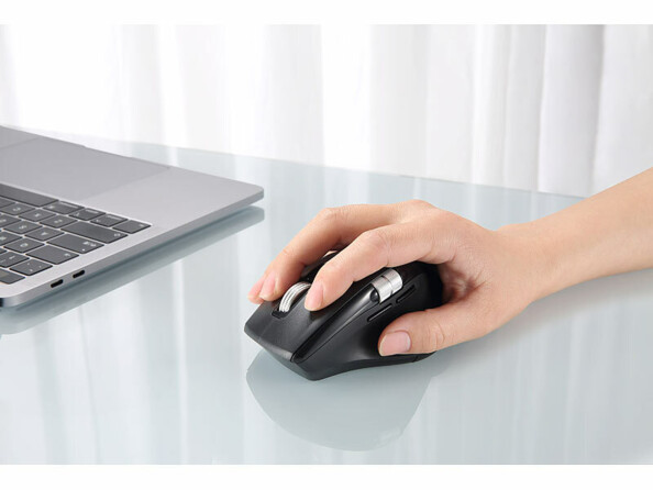 Prise en main de la souris optique sans fil multi-appareils pour droitier sur une table en verre fumé à côté d'un PC portable