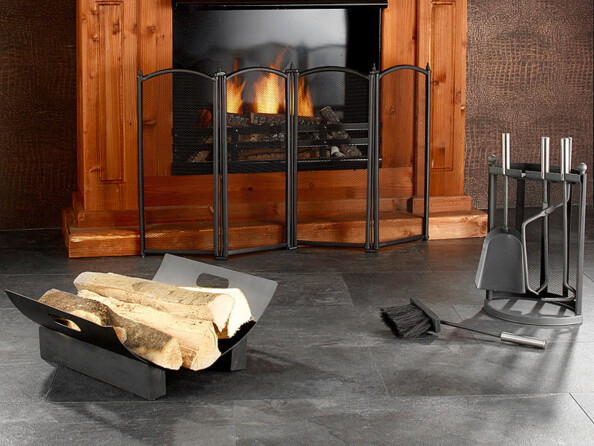 Mise en situation du serviteur 4 pièces, de la grille pare-étincelles et du range-bûches devant une cheminée bien entretenue dans laquelle un feu est allumé dans un salon moderne