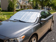 Housse de protection de pare-brise réfléchissante couvrant une Renault Captur bicolore (gris argenté et noir). L'image est divisée verticalement, montrant une scène d'été verdoyante à gauche et une scène d'hiver enneigée à droite. Un bandeau de texte cent