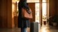 Mise en situation d'une femme en manteau dans un hall avec valise devant elle et sac à main en cuir sur l'épaule droite entrain de ranger la batterie de secours