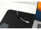 Cordon blanc USB maintenu en ordre par un cube magnétique passe-câble lesté sur un tapis de souris de la même couleur à côté d'un iPhone et d'un Mac