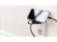 Smartphone type iPhone éteint, branché à un chargeur secteur noir branché à une prise de courant via câble USB et posé contre la boucle de support du chargeur contre le mur