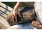 Insertion d'un smartphone en cours de chargement dans une poche latérale extérieure du sac à dos avec panneau solaire par un homme en short et t-shirt assis sur un banc