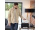 Homme en jean, t-shirt blanc et chemise beige brun barbu sortant une impression de son imprimante wifi Brother coloris noir installée dans un salon moderne avec baie vitrée anthracite, mur blanc et mur en briques rouges