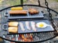 Mise en situation de 2 plaques de cuisson 51 cm sur une grille de barbecue au charbon, cuisinant des oeufs et du bacon sur le côté lisse et de la viande sur la plaque côté rainuré 