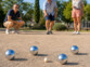Partie de pétanque en plein air avec quatre boules métalliques autour du cochonnet et trois personnes en train de jouer