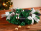Couronne de l'Avent coloris argenté posée sur une table de salon en bois à côté de noix entières devant un sapin de Noël décoré de guirlandes lumineuses et décorations de Noël