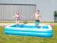Un garçon et une fille en maillots de bain en train de sauter dans la pataugeoire Speeron dans un jardin en extérieur
