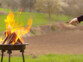 Mise en situation d'une personne cuisant une saucisse piquée sur la brochette au barbecue 