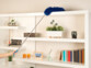 Main époussetant des étagères avec un plumeau télescopique bleu dans un intérieur avec livres et plantes