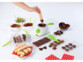 Chocolatière blanche et vert anis entourée de nombreuses préparations chocolatées : biscuits, pralines, fruits nappés de chocolat, petits chocolats, etc.