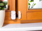 Mise en situation de l'alarme placée sur une fenêtre en bois marron clair, ouverte par un cambrioleur, avec capteur magnétique détachée de l'unité centrale de l'alarme à une distance de quelques centimètres