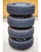 4 pneus de jantes alignés et rangés de manière ordonné sur le support de stockage automobile HP Autozubehör dans un garage avec sol en béton et mur en lambris de bois clair