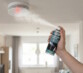 ne personne vaporise le spray de test STANGER vers un détecteur de fumée fixé au plafond d'un salon, déclenchant le voyant lumineux rouge de l'appareil."