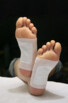 Mise en situation de deux pads au bambou collés sur les pieds d'une personne ayant les jambes croisées