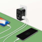 Deux smartphones posés sur une surface vert sapin en cours de chargement par le biais de deux câbles USB branchés aux deux ports de chargement du chargeur secteur universel branché à une prise secteur d'un mur blanc