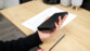 Calculatrice électronique fermée tenue en main par une personne se tenant au-dessus d'un bureau en bois clair