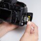 Main insérant une carte mémoire SDXC PNY à deux doigts dans la fente pour carte mémoire d'un appareil photo reflex noir éteint tenu dans une autre main