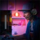 Jeune homme en sweat et casquette portant le casque stéréo Spirit of Gamer sur la tête pendant une séance de gaming sur PC dans une chambre à l'éclairage tamisée violet/bleu