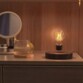 Ampoule bulbe en lévitation allumée sur son socle électromagnétique aspect bois sur une coiffeuse sur laquelle sont posés un miroir et une tasse de thé avec dessous de verre