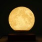 Lune lumineuse rétroéclairée d'une lumière jaune chaud en lévitation sur une base électromagnétique dans le noir