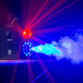 Fumigène bleuté émis dans un débit puissant par la machine à fumée F700 FX BoomToneDJ sur une estrade d'une salle de spectacle accompagné d'une lumière rouge à faisceaux lumineux multiples