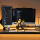 Figurine Bumblebee programmable en garde poings fermés sur un bureau devant deux écrans d'ordinateur affichant des lignes de code