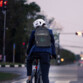 Mise en situation d'un cycliste arrêté sur la route le soir à un feu rouge et indiquant par le biais de son sac à dos qu'il tourne à gauche