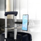 Smartphone allumé fixé à la pince de fixation extensible du support pour téléphone portable accroché à la poignée d'une valise dans le hall d'un aéroport
