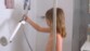 Petite fille dans une douche prenant en main le pommeau de douche tenu par le support pour douchette ShowerXtend fixé par ventouse à une des parois de la douche