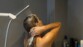 Mise en situation d'une femme nue aux cheveux longs bruns prenant sa douche avec le bras de support maintenant le pommeau de douche au-dessus de sa tête dont les cheveux sont plein de savon