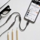 Câble adaptateur Lightning vers double jack branché à un iPhone affichant une playlist musical posé à côté d'une paire de lunettes et de trois crayons 