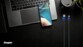 Câble USB-A vers Lightning bicolore Energizer posé à côté d'un MacBook ouvert, d'un iPhone allumé et d'une tasse de café vide sur un fond sombre