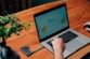 Mini disque dur externe SSD Verbatim branché par mini câble USB-C au port USB-C d'un PC portable Windows sur lequel travaille une personne installée à une table en bois sur laquelle est posée une plante en pot