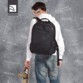 Jeune homme en jean et t-shirt blanc avec oreillette à l'oreille de dos portant le sac à dos Lato Tucano coloris noir