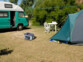Batterie de secours Revolt posée sur un sol terreux, branchée à l'intérieur d'un camping et dans une tente par deux longs câbles de raccordement en extérieur