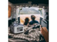 Mise en situation de la batterie nomade Revolt à l'arrière un van, sur une couverture, à côté d'une guitare et derrière un couple homme-femme assis par terre et observant la vue sur un canyon