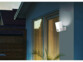 Mise en situation de la caméra de sécurité fixée à la façade d'une maison à côté d'une porte-fenêtre dans l'obscurité avec projecteur LED allumé