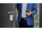Homme en costume bleu entrain dans une propriété par déverrouillage de la serrure de domotique connectée et intelligente par application sur son smartphone