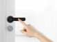 Main d'une personne faisant le code PIN d'accès sur la poignée de porte noire pour déverrouiller la porte blanche sur laquelle elle est installée
