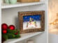 Cadre décoratif de Noël "Bonhommes de neige" posé sur une étagère blanche à côté d'une décoration de Noël avec branches de sapin et boules rouges brillantes
