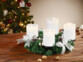 Couronne de l'Avent coloris argenté avec 4 bougies LED coloris blanc posée sur une table de salon en bois à côté de noix entières devant un sapin de Noël décoré de guirlandes lumineuses et décorations de Noël