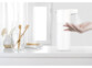 Mise en situation du distributeur de savon sur un meuble d'une salle de bain blanc avec divers accessoires de beauté et la main d'une personne se servant en savant en passant la main sous le détecteur