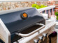 Thermomètre filaire installé sur le couvercle d'un barbecue au gaz moderne avec écran rond orange indiquant la température à coeur des aliments cuisant à l'intérieur ainsi que la température de l'espace de cuisson