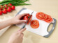 Personne découpant une tomate avec un couteau sur la planche moyenne posée sur un plan de travail à côté de légumes