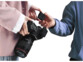 Une personne en t-shirt bleu donne le boîtier émetteur à une personne avec blouson rose pâle tenant un appareil photo professionnelle en main