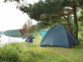 Chaise de camping noire et bleue dépliée devant une tente vert sapin montée devant un plan d'eau sous un arbre