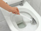 Main d'une personne tenant le balai WC en nettoyant la cuvette des toilettes